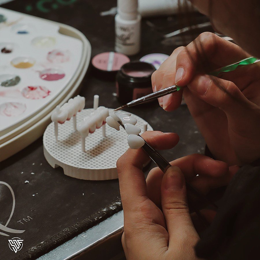 Ceramist staining a restoration by hand at the bench